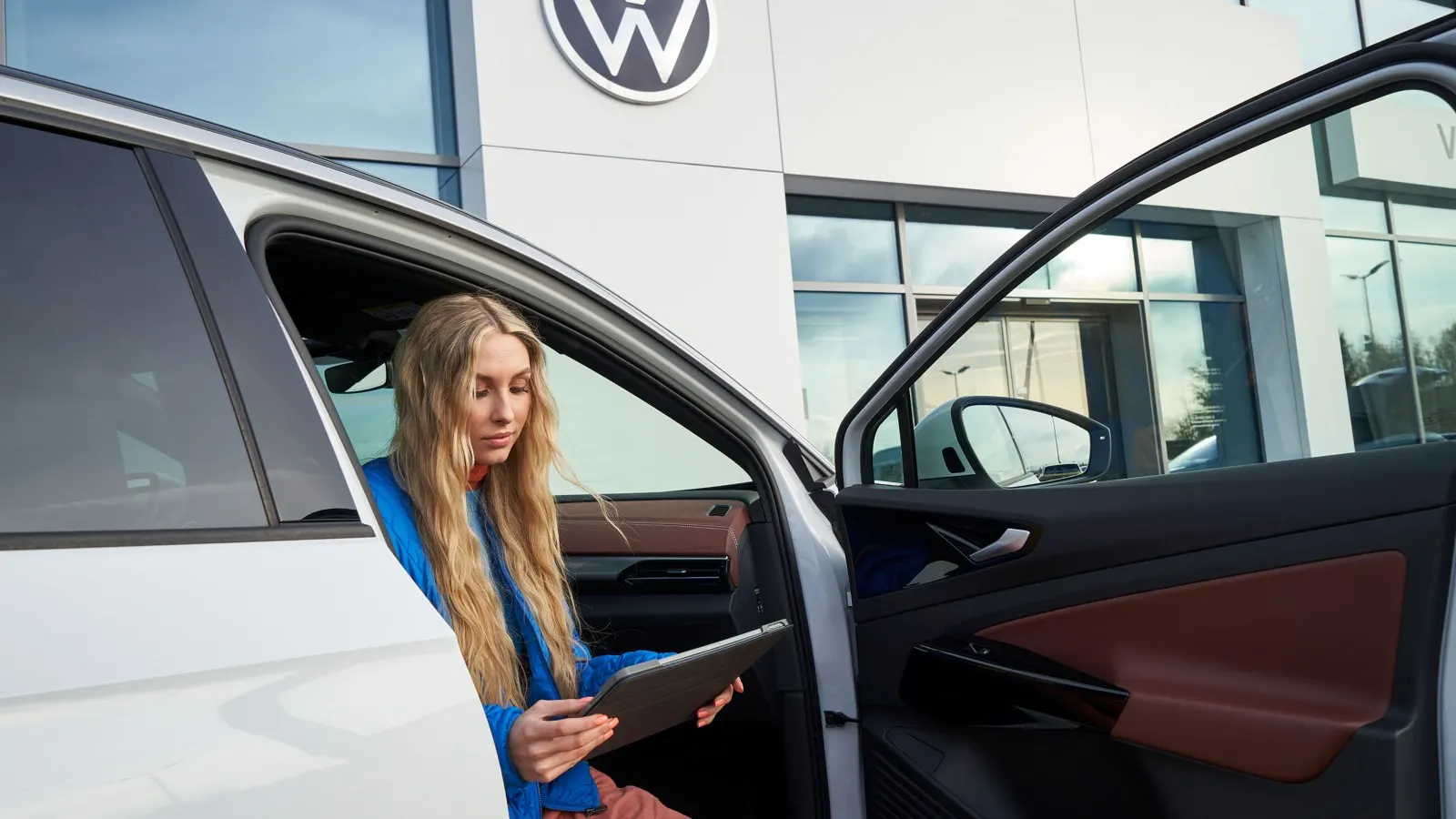 Fahrerin sitzt mit Tablet in einem VW ID. vor einem Volkswagen-Autohaus